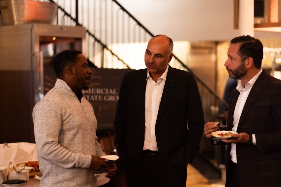 Three members talking over appetizers beside the welcome sign