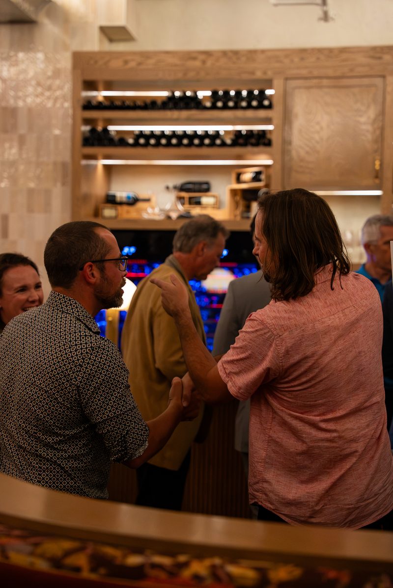 Two members shaking hands at the bar, with the wine wall behind them
