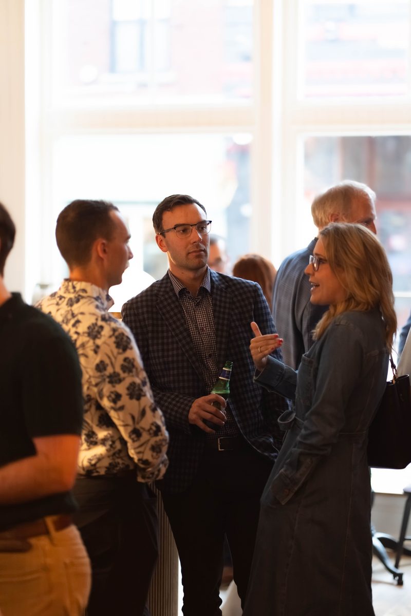 Members in conversation beside a tall window early in the evening
