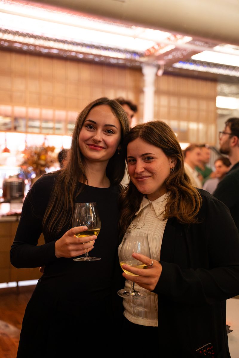 Two members posing with glasses of wine near the bar