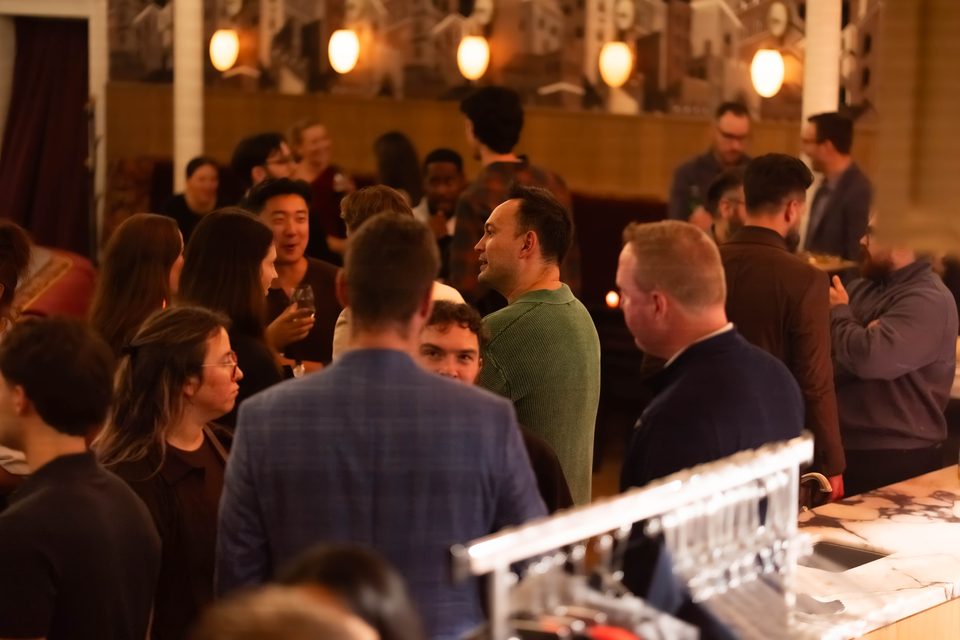 The crowded room seen from behind the bar, with glasses lined up in the foreground