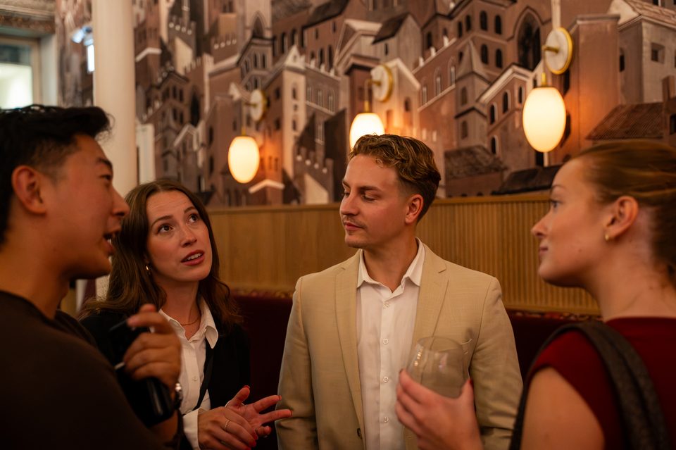 Four members in conversation beneath the mural, with a lamp glowing beside them