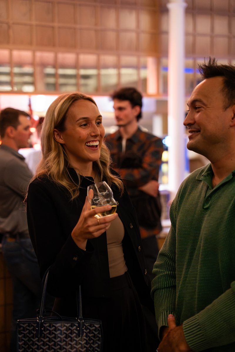 Two members laughing together in conversation, glasses in hand