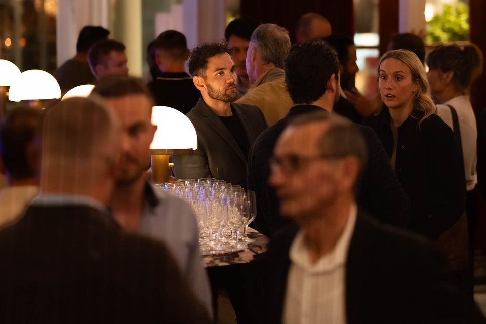 Members in conversation with a tray of wine glasses in the foreground