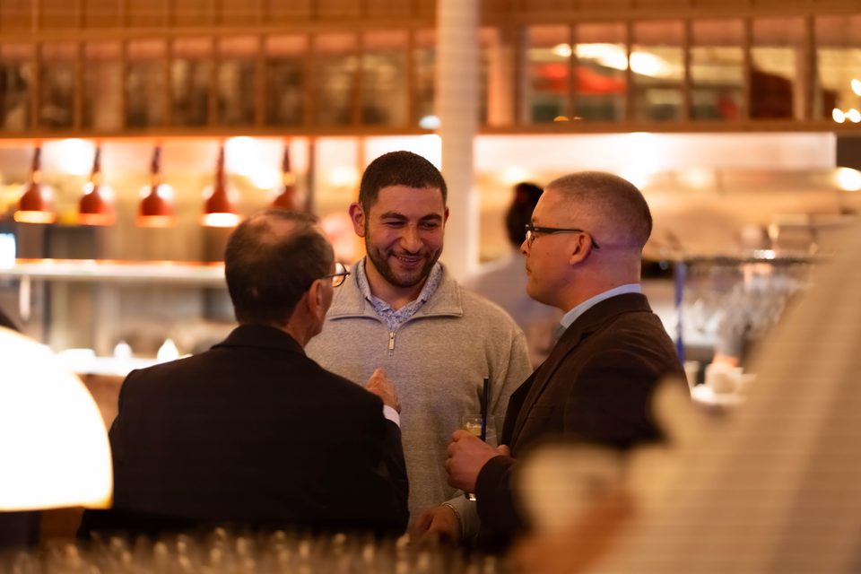 Two members laughing together at the kitchen pass, with copper lamps overhead