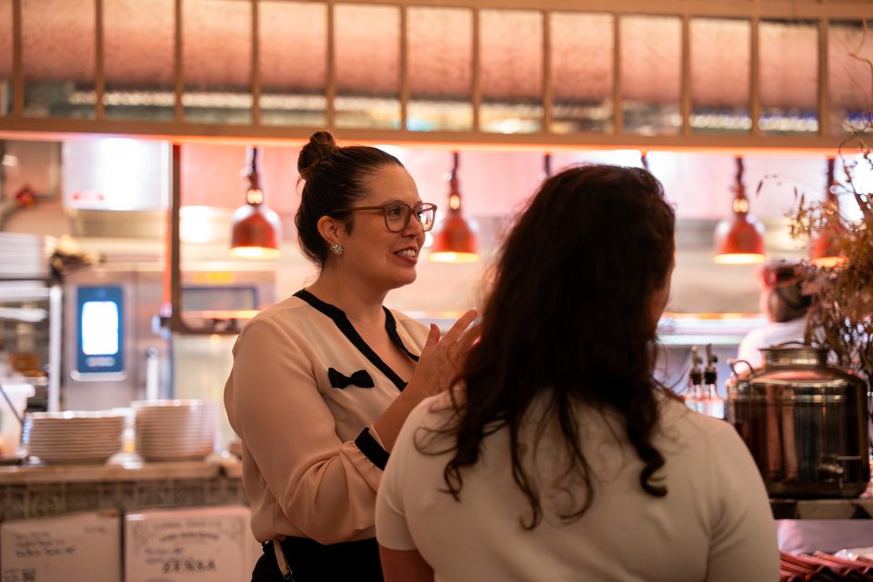 Two members talking at the kitchen pass under the copper lamps