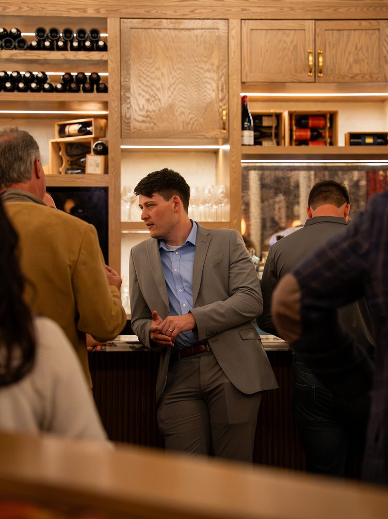 A member in a grey suit in conversation beside the bar