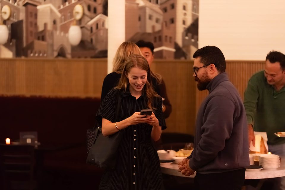 A member checking her phone while a group talks beside the appetizer table