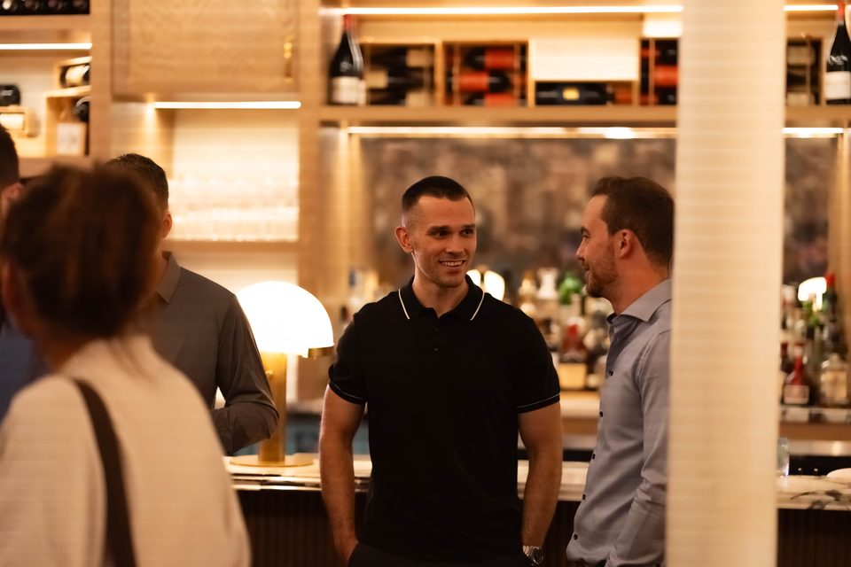 A member in conversation at the bar, with bottles and glassware on the shelves behind