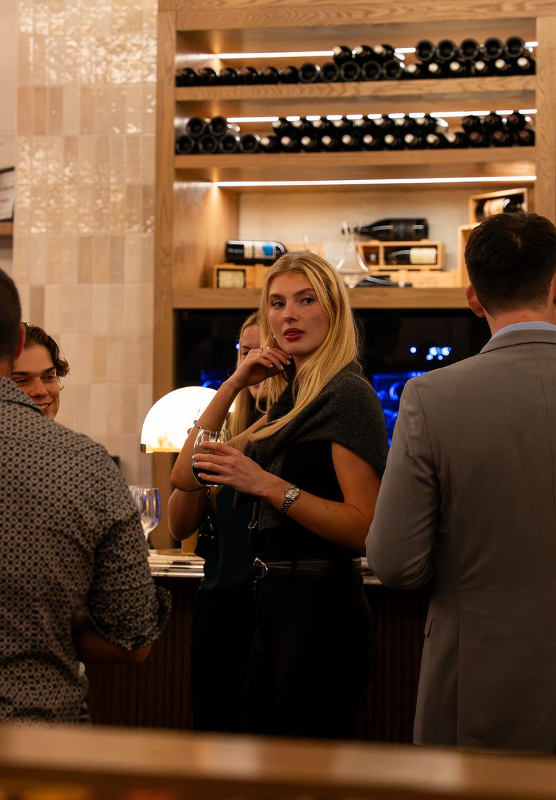 A member in conversation at the bar later in the evening, with the wine wall behind