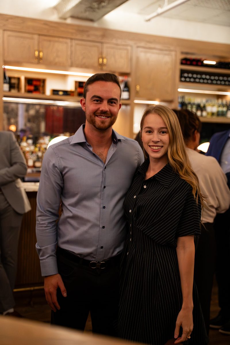 Two members posing for a photo in front of the bar shelves