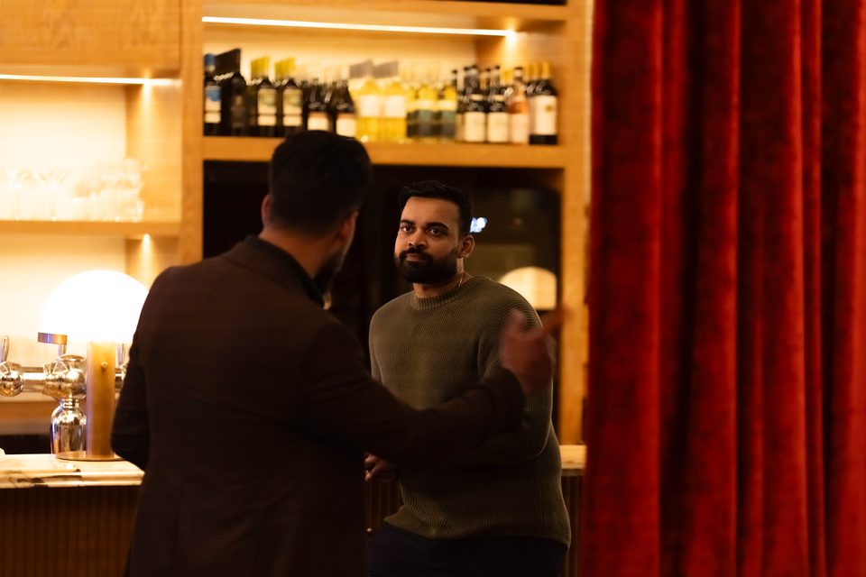 Two members talking beside the red curtain and the bar shelves