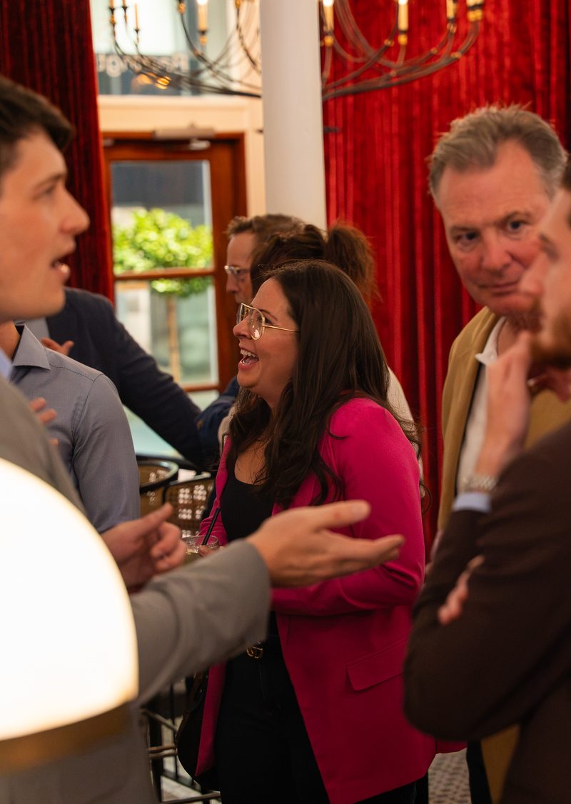 A group in animated conversation beside the red curtain and the window