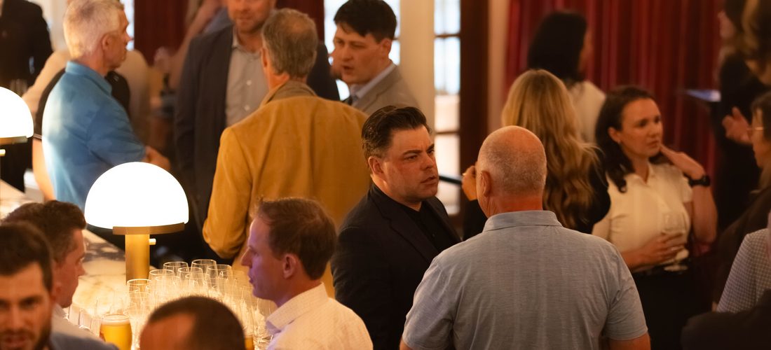 A full room of members in conversation at the Halifax mixer, under warm lamps with a bar in the foreground